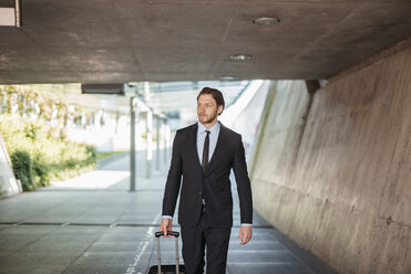 Businessman with rolling suitcase walking in underpass - DIGF04838