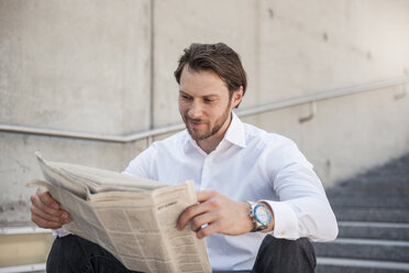 Smiling businessman sitting on stairs reading newspaper - DIGF04855