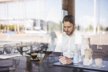 Businessman behind windowpane using tablet in a cafe - DIGF04860