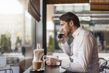 Businessman with tablet in a cafe drinking coffee from glass - DIGF04863