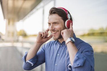 Porträt eines glücklichen Mannes, der mit Kopfhörern Musik hört - DIGF04872