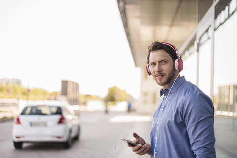Lächelnder Mann, der mit Kopfhörern im Freien Musik hört, lizenzfreies Stockfoto