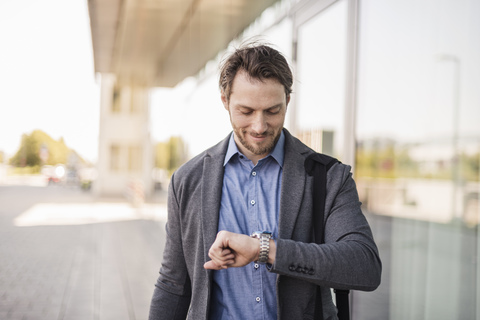 Lächelnder Geschäftsmann mit Laptoptasche, der die Zeit überprüft, lizenzfreies Stockfoto