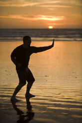 Ein mittelgroßer Mann übt Taekwondo am Strand von Morro Bay, Kalifornien, bei Sonnenuntergang. - AURF00527