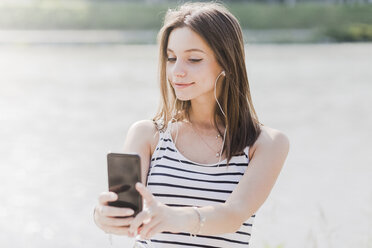 Smiling young woman with smartphone and earphones at the waterfront - GIOF04135