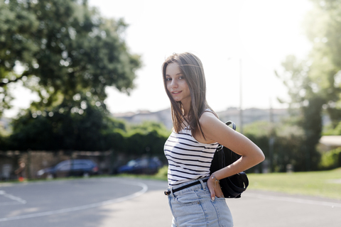 Porträt einer lächelnden jungen Frau mit Rucksack im Freien im Sommer, lizenzfreies Stockfoto