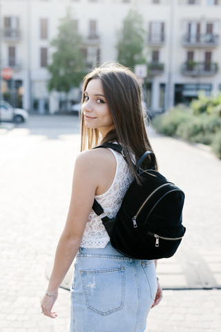 Porträt einer lächelnden jungen Frau mit Rucksack in der Stadt, lizenzfreies Stockfoto