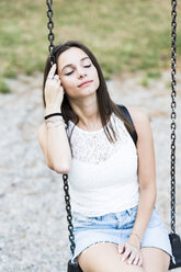 Junge Frau mit geschlossenen Augen sitzt auf einer Schaukel auf einem Spielplatz - GIOF04166