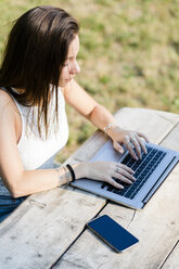 Junge Frau benutzt Laptop auf Holztisch im Freien - GIOF04169