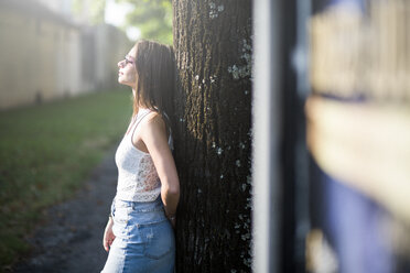 Young woman wearing sunglasses leaning against a tree trunk - GIOF04175