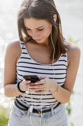 Junge Frau mit Smartphone und Kopfhörern an der Uferpromenade - GIOF04177