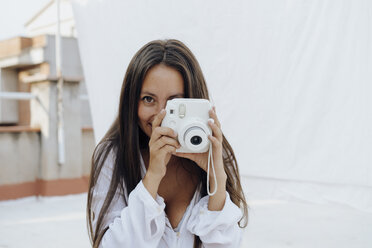 Portrait of young woman taking photos with camera on roof terrace - AFVF01412