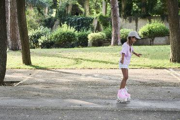 Kleines Mädchen mit Zöpfen und Mütze beim Rollschuhlaufen im Park - IGGF00509