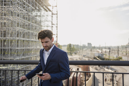 Geschäftsmann steht auf einer Brücke in der Stadt und benutzt ein Mobiltelefon - DIGF04878