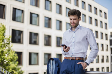 Businessman standing in the city using cell phone - DIGF04884