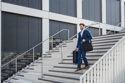 Lächelnder Geschäftsmann mit Gepäck in der Stadt, der eine Treppe hinuntergeht, lizenzfreies Stockfoto