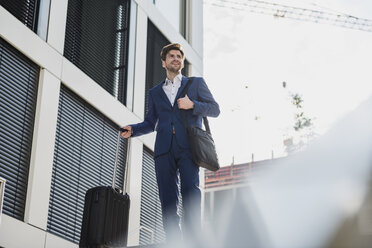 Smiling businessman with baggage in the city looking around - DIGF04901