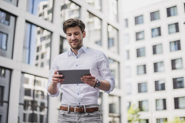 Smiling businessman in the city using tablet - DIGF04912