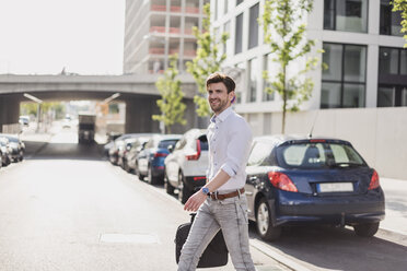 Smiling businessman with laptop bag in the city crossing the street - DIGF04914