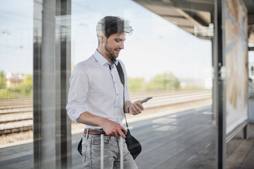 Geschäftsmann mit Gepäck, der auf dem Bahnsteig steht und ein Mobiltelefon benutzt - DIGF04915