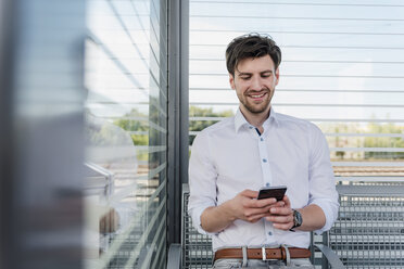 Smiling businessman on station platform using cell phone - DIGF04918