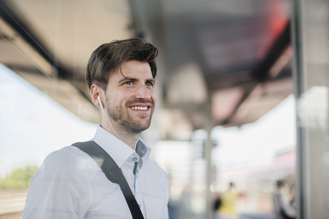 Porträt eines lächelnden Geschäftsmannes auf einem Bahnsteig mit Kopfhörern, lizenzfreies Stockfoto