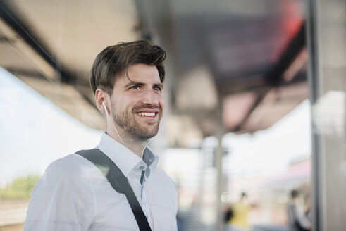 Porträt eines lächelnden Geschäftsmannes auf einem Bahnsteig mit Kopfhörern - DIGF04921