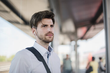 Portrait of businessman on station platform with earphones - DIGF04922