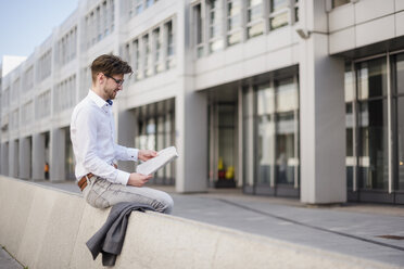 Businessman sitting in the city reading newspaper - DIGF04923