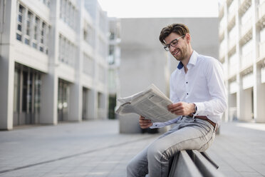 Lächelnder Geschäftsmann sitzt in der Stadt und liest Zeitung - DIGF04924