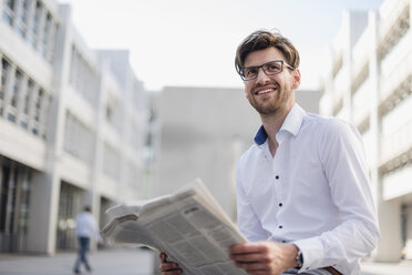 Lächelnder Geschäftsmann sitzt in der Stadt und liest Zeitung - DIGF04925