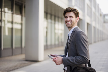 Smiling businessman in the city with bag and tablet - DIGF04934