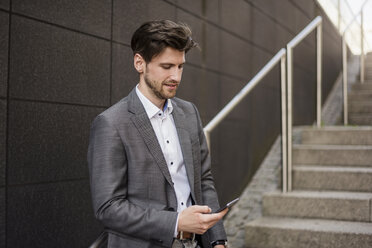 Businessman using cell phone on stairs - DIGF04939