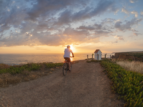 Portugal, Alentejo, älterer Mann auf E-Bike bei Sonnenuntergang, lizenzfreies Stockfoto