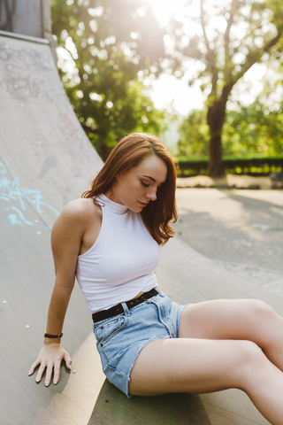 Rothaarige Frau sitzt bei Sonnenuntergang in einem Skatepark, lizenzfreies Stockfoto