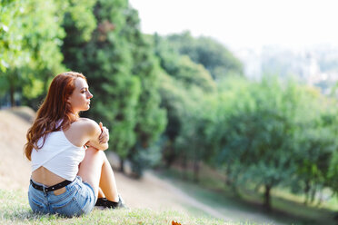 Rothaarige Frau entspannt sich auf einem Hügel in einem Park - GIOF04204