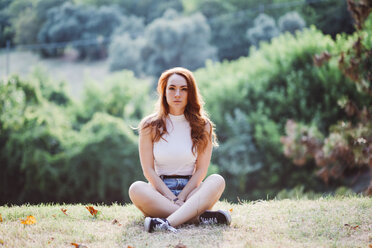 Italy, Verona, portrait of serious redheaded woman sitting on a meadow - GIOF04206