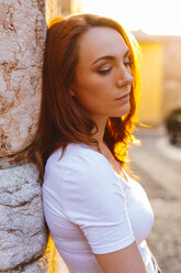 Portrait of redheaded woman leaning against wall at sunset - GIOF04219