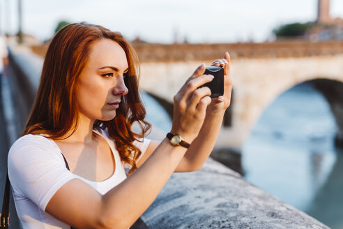 Italien, Verona, rothaarige Frau fotografiert mit Smartphone - GIOF04228