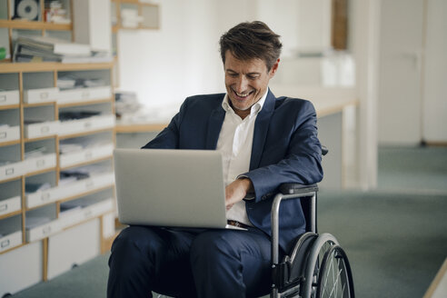 Geschäftsmann im Rollstuhl, der im Büro einen Laptop benutzt - GUSF00978