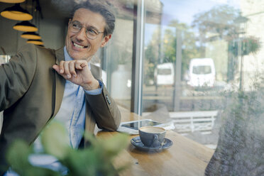 Mature businessman sitting in coffee shop, smiling - GUSF00987