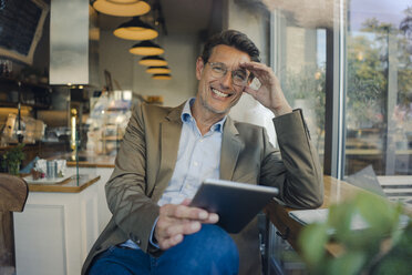 Älterer Geschäftsmann, der in einem Café sitzt und ein digitales Tablet benutzt - GUSF00989