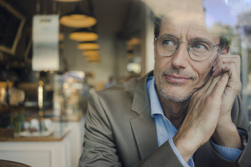 Älterer Geschäftsmann sitzt in einem Café und schaut aus dem Fenster - GUSF00990