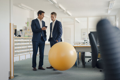 Zwei Geschäftsleute überprüfen ihr Smartphone mit einem gelben Fitnessball im Vordergrund - GUSF00994