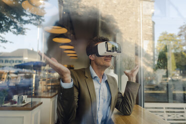 Älterer Geschäftsmann sitzt in einem Café und schaut durch eine VR-Brille - GUSF00995