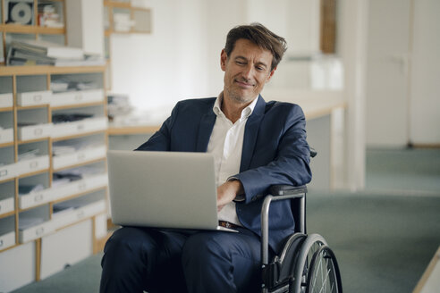 Geschäftsmann im Rollstuhl, der im Büro einen Laptop benutzt - GUSF01012