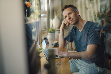 Mid adult man sitting in coffee shop, using laptop - GUSF01017