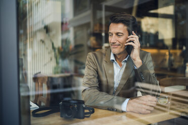 Älterer Geschäftsmann sitzt in einem Café und spricht am Telefon - GUSF01031