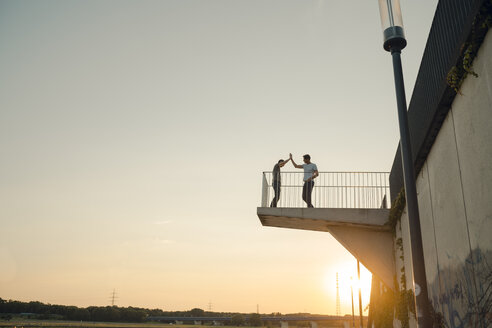 Two friends high-fiving at sunset, standing on observation platform - GUSF01036