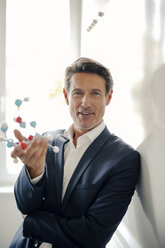 Successful businessman leaning on whiteboard, holding molecule model - GUSF01060